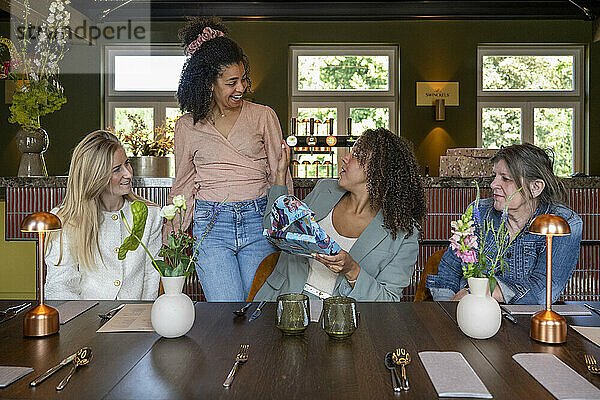 Group of women enjoying a conversation at a well-set dining table with elegant decor and warm lighting.