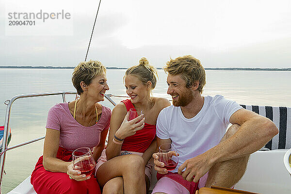 Three friends enjoy drinks and conversation on a boat with a serene lake in the background.