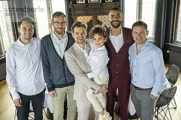 A group photo of five smiling men and a young boy indoors  dressed in smart casual attire.