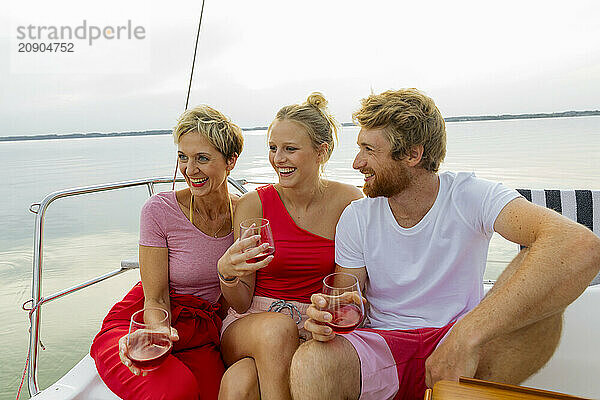 Three friends enjoying drinks and laughter on a boat with a tranquil water background.