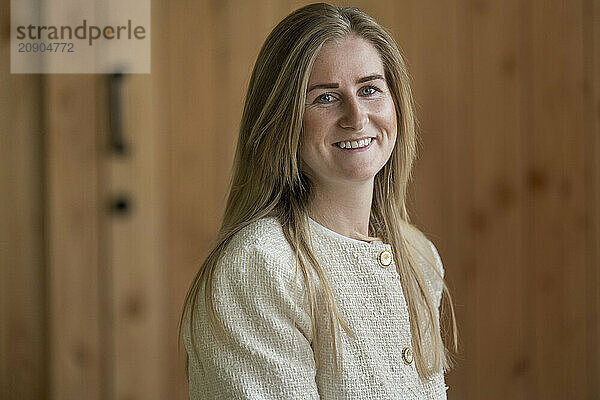 Smiling young woman in a white jacket standing against a wooden wall background