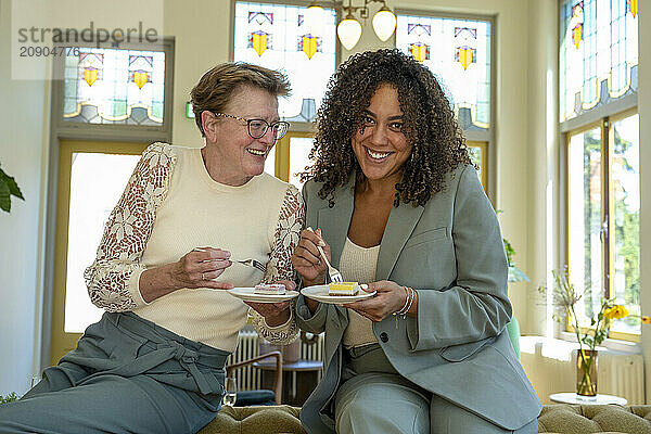 Two women smiling  enjoying tea and cake in a room with stained glass windows.