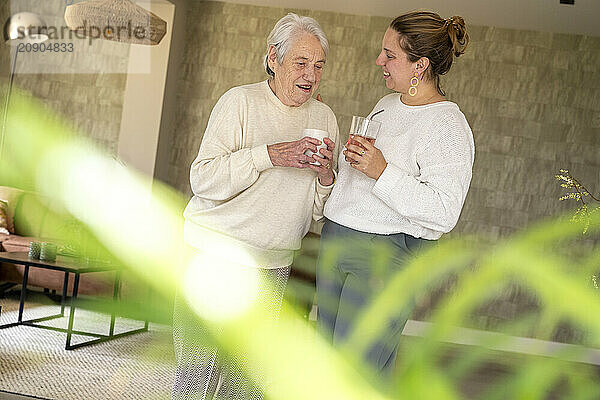 Elderly woman and young adult having a conversation over drinks in a cozy living room.