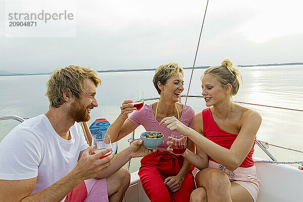 Three friends enjoying drinks and snacks on a boat during a sunny day with a clear sky and a calm lake in the background.