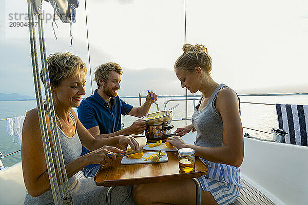 Friends enjoy a meal together on a sailboat at sunset with a picturesque view of the water.