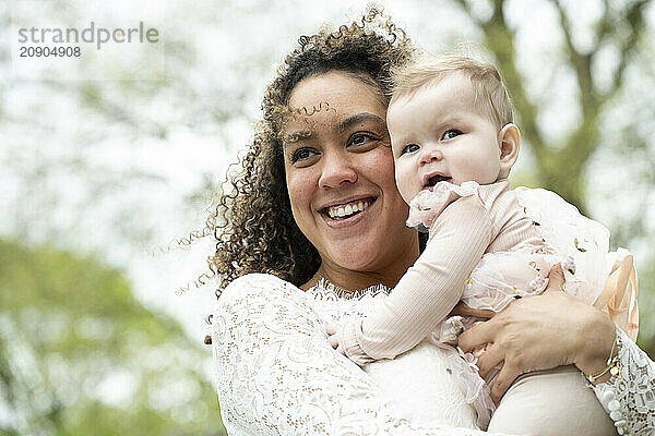 A joyful woman holding a baby girl outdoors  both smiling against a natural backdrop.