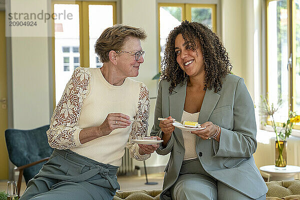 Two women enjoying cake together in a well-lit room with a pleasant atmosphere.