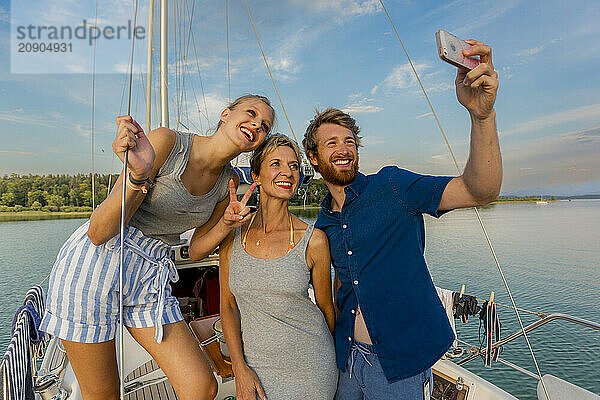 Three friends taking a selfie on a sailboat with a clear blue sky in the background.