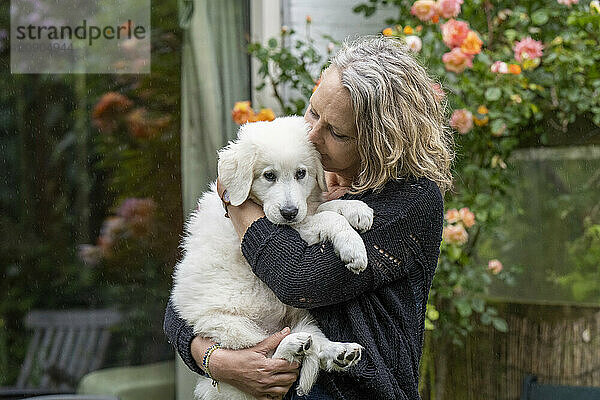 Woman embracing a white puppy in a garden with blooming roses.