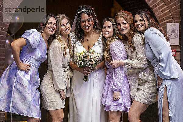 Bride in a white dress smiling with her bridesmaids in pastel dresses holding a bouquet of flowers.