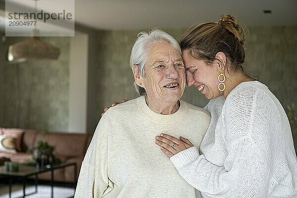 Elderly woman and young adult female embracing and smiling in a cozy living room.