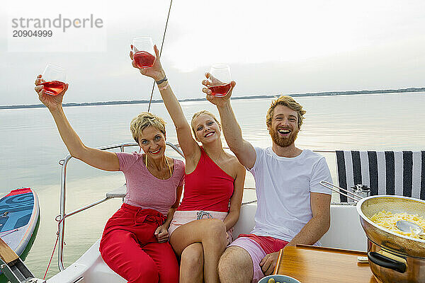 Three friends enjoying drinks and laughter on a boat with a serene lake in the background.