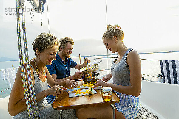 Friends enjoy a meal on a sailboat with scenic water and skyline views at dusk.