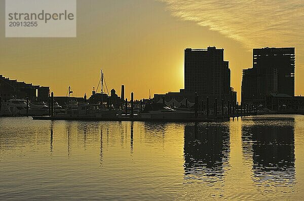 A dramatic and beautiful sunrise with buildings and boats in silhouette reflected in the waters of Baltimore's Inner Harbor Harbour Maryland  USA  North America