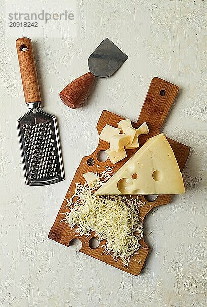 Geriebener Käse  Maasdam  auf einem Schneidebrett  Reibe und Käsemesser  Nahaufnahme  keine Personen