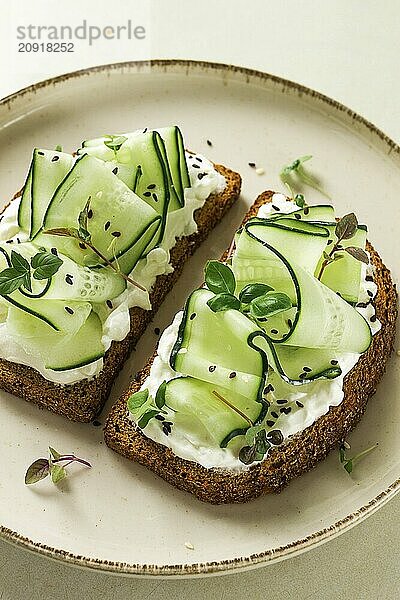 Frühstück  Müslibrötchen  Frischkäse  Gurkenscheiben  mit Mikrogrün auf einem hellen Tisch  Nahaufnahme  Draufsicht  selektiver Fokus  keine Personen