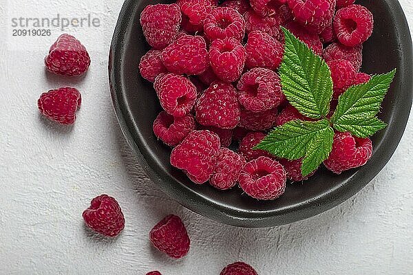 Frische Himbeeren  auf einem schwarzen Teller  mit Blättern  Draufsicht  auf einem weißen Tisch