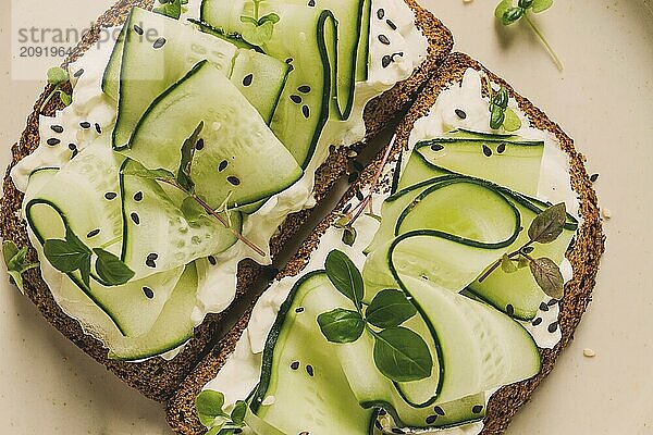 Frühstück  Müslibrötchen  Frischkäse  Gurkenscheiben  mit Mikrogrün auf einem hellen Tisch  Nahaufnahme  Draufsicht  selektiver Fokus  keine Personen