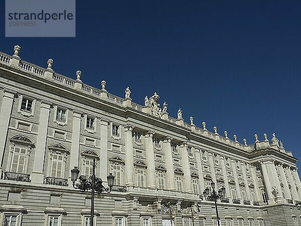 Wide frontal view of a classical baroque building with numerous windows and sculptures under a blue sky  Madrid  Spain  Europe