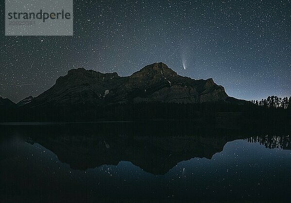 Night sky with stars over a mountain and its reflection in a calm lake  silhouette and a visible comet  Comet Neowise  Kananaskis Country  Alberta  Canada  North America