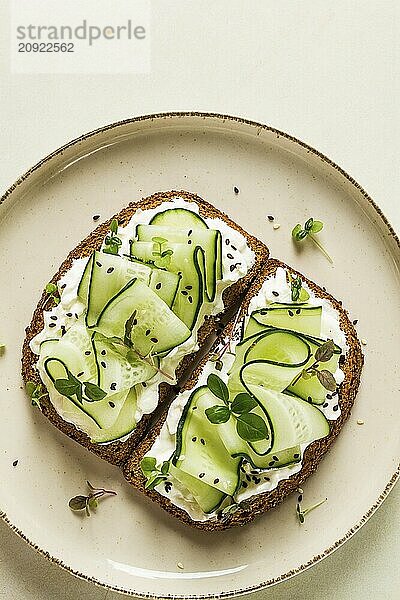 Frühstück  Müslibrötchen  Frischkäse  Gurkenscheiben  mit Mikrogrün auf einem hellen Tisch  Nahaufnahme  Draufsicht  selektiver Fokus  keine Personen