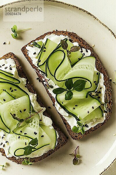 Frühstück  Müslibrötchen  Frischkäse  Gurkenscheiben  mit Mikrogrün auf einem hellen Tisch  Nahaufnahme  Draufsicht  selektiver Fokus  keine Personen