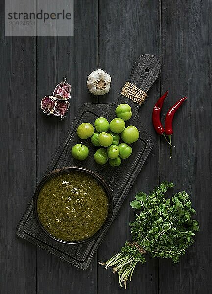 Tkemali Sauce  traditionelle georgische Küche  grüne Kirschpflaume  mit Zutaten für die Sauce  Koriander  Minze  scharfer Pfeffer  Knoblauch  auf einem Holztisch  Nahaufnahme  rustikal  Lebensmittel Hintergrund  keine Menschen  selektiver Fokus  Sauce  grüne Sauce  tkemali  georgische Küche  hausgemacht