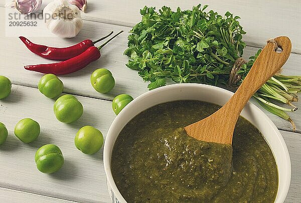 Tkemali Sauce  traditionelle georgische Küche  grüne Kirschpflaume  mit Zutaten für die Sauce  Koriander  Minze  Paprika  Knoblauch  auf einem weißen Holztisch  Nahaufnahme  rustikal  Lebensmittel Hintergrund  keine Menschen  selektiver Fokus  Sauce  grüne Sauce  tkemali  georgische Küche  hausgemacht