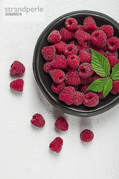 Frische Himbeeren  auf einem schwarzen Teller  mit Blättern  Draufsicht  auf einem weißen Tisch