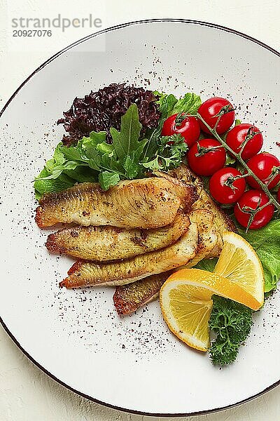 Gebratenes Tilapia Fischfilet  in Gewürzen  mit Kirsche und Salat  auf einem weißen Teller  hausgemacht  ohne Personen