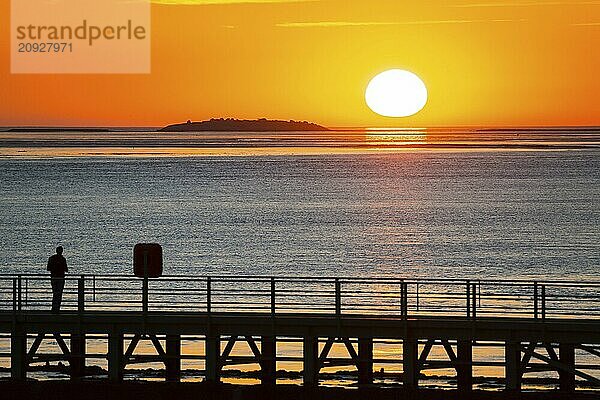 Silhouette of a person on the pier Freilaufkanal  person watching from a jetty the picturesque  golden  breathtakingly beautiful sunset over the sea  island Langlütjen II far away  sun ball just above the horizon  orange glowing cloudless sky  wide sea in soft colours  calm atmosphere  mouth of the Weser into the North Sea  Outer Weser  Bremerhaven  Land Bremen  Germany  Europe