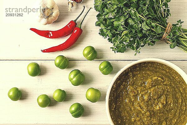 Tkemali Sauce  traditionelle georgische Küche  grüne Kirschpflaume  mit Zutaten für die Sauce  Koriander  Minze  Paprika  Knoblauch  auf einem weißen Holztisch  Nahaufnahme  rustikal  Lebensmittel Hintergrund  keine Menschen  selektiver Fokus  Sauce  grüne Sauce  tkemali  georgische Küche  hausgemacht