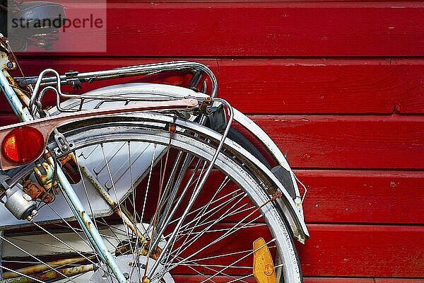 Zwei alte Fahrräder lehnen an einer roten Holzwand