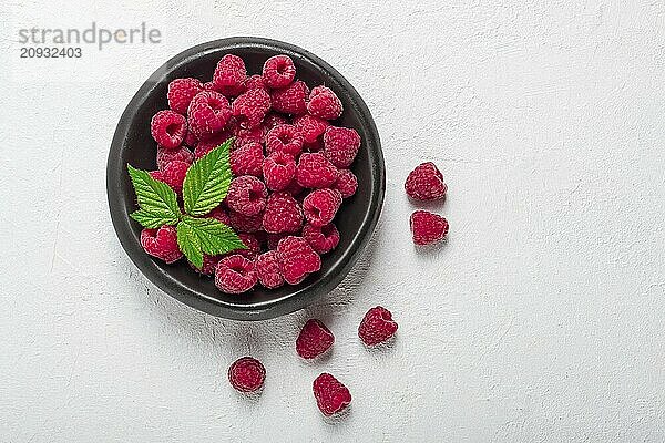 Frische Himbeeren  auf einem schwarzen Teller  mit Blättern  Draufsicht  auf einem weißen Tisch