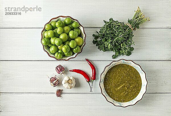 Tkemali Sauce  traditionelle georgische Küche  grüne Kirschpflaume  mit Zutaten für die Sauce  Koriander  Minze  Paprika  Knoblauch  auf einem weißen Holztisch  Nahaufnahme  rustikal  Lebensmittel Hintergrund  keine Menschen  selektiver Fokus  Sauce  grüne Sauce  tkemali  georgische Küche  hausgemacht