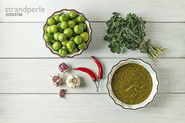 Tkemali Sauce  traditionelle georgische Küche  grüne Kirschpflaume  mit Zutaten für die Sauce  Koriander  Minze  Paprika  Knoblauch  auf einem weißen Holztisch  Nahaufnahme  rustikal  Lebensmittel Hintergrund  keine Menschen  selektiver Fokus  Sauce  grüne Sauce  tkemali  georgische Küche  hausgemacht