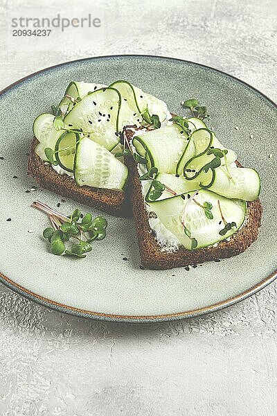 Frühstück  Müslibrötchen  Frischkäse  Gurkenscheiben  mit Mikrogrün auf einem hellen Tisch  Nahaufnahme  Draufsicht  selektiver Fokus  keine Personen