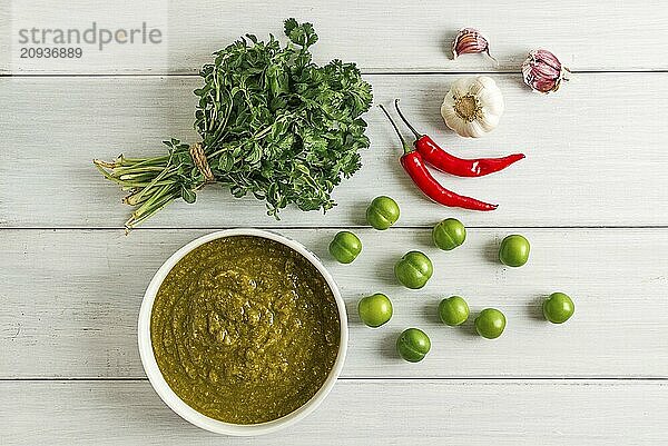 Tkemali Sauce  traditionelle georgische Küche  grüne Kirschpflaume  mit Zutaten für die Sauce  Koriander  Minze  Paprika  Knoblauch  auf einem weißen Holztisch  Nahaufnahme  rustikal  Lebensmittel Hintergrund  keine Menschen  selektiver Fokus  Sauce  grüne Sauce  tkemali  georgische Küche  hausgemacht