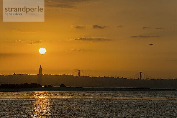 Romantischer Sonnenuntergang mit Silhouetten einer Brücke und eines Flugzeugs am Abendhimmel über dem Wasser  Statue Cristo Rei  Ponte 25 de Abril  Brücke des 25. April  Hängebrücke über den Tejo  Lissabon  Lisboa  Portugal  Europa