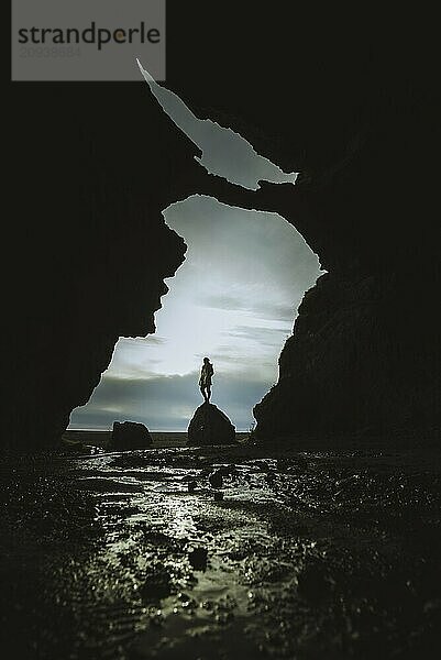 Dramatic silhouette of a person standing in a cave opening with ocean view and twilight sky  Southwest  Iceland  Europe