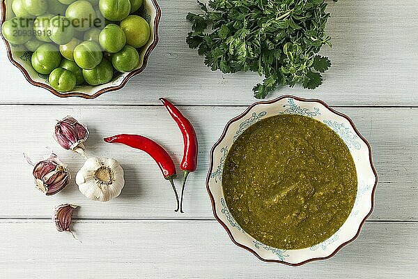 Tkemali Sauce  traditionelle georgische Küche  grüne Kirschpflaume  mit Zutaten für die Sauce  Koriander  Minze  Paprika  Knoblauch  auf einem weißen Holztisch  Nahaufnahme  rustikal  Lebensmittel Hintergrund  keine Menschen  selektiver Fokus  Sauce  grüne Sauce  tkemali  georgische Küche  hausgemacht