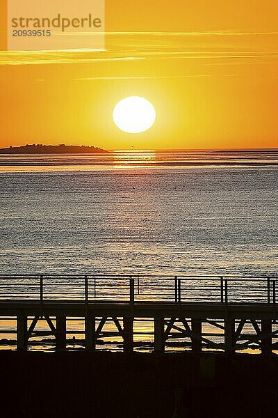 Silhouette of a jetty  pier free canal  in front of a picturesque  golden  breathtakingly beautiful sunset over the sea  island Langlütjen II far away  sun ball just above the horizon  orange glowing cloudless sky  wide sea in soft colours  calm atmosphere  mouth of the Weser into the North Sea  Outer Weser  Bremerhaven  Land Bremen  Germany  Europe