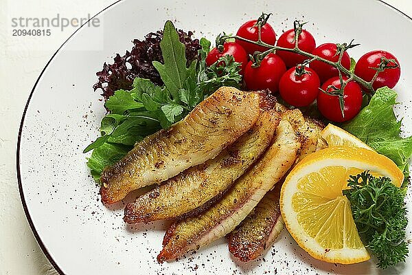 Gebratenes Tilapia Fischfilet  in Gewürzen  mit Kirsche und Salat  auf einem weißen Teller  hausgemacht  ohne Personen