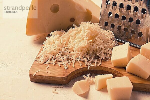 Geriebener Käse  Maasdam  auf einem Schneidebrett  Reibe und Käsemesser  Nahaufnahme  keine Personen