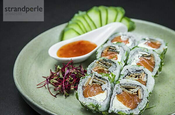 Perfektes Sushi  traditionelle japanische Küche. Leckere Uramaki mit süß saurer Soße auf dem dekorierten Teller  schwarzer Hintergrund