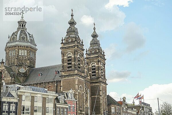 Frontansicht einer großen Kirche mit zwei Türmen und umliegenden Gebäuden unter einem leicht bewölkten Himmel mit Fahnen im Vordergrund  Amsterdam  niederlande