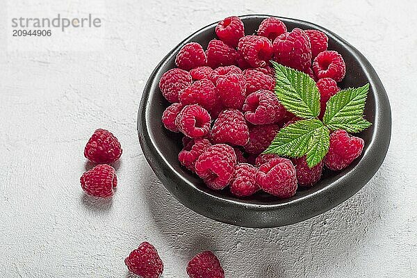 Frische Himbeeren  auf einem schwarzen Teller  mit Blättern  Draufsicht  auf einem weißen Tisch