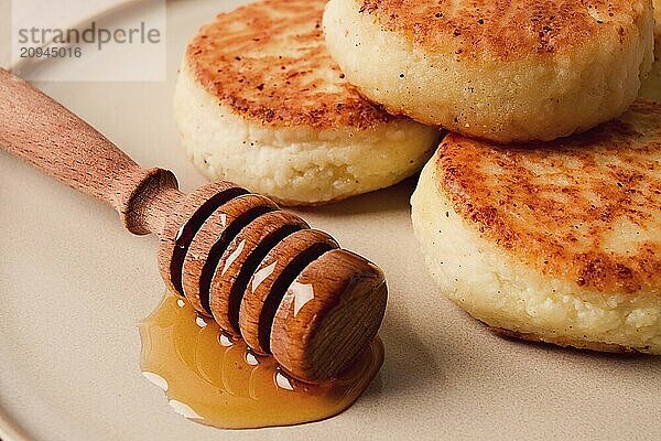 Hüttenkäsepfannkuchen  mit Honig  Nahaufnahme  auf einem beigen Tisch  selektiver Fokus  keine Personen