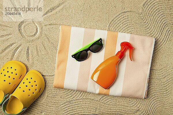 Zeichnung auf dem Sand  Sonne und Wellen  Sonnenbrille  mit orangefarbener Flasche  gelbe Gummipantoffeln  Strandtuch  Sonnenspray  auf dem Sand  Draufsicht  ohne Menschen