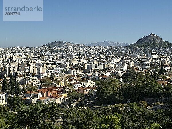 City silhouette with various houses in front of a hilly background  Ancient buildings with columns and trees on the Acropolis in Athens in front of a blue sky  athens  greece